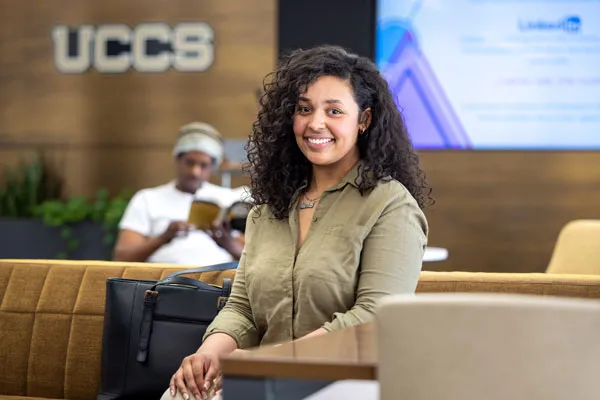 UCCS student sitting in front off a UCCS logo sign